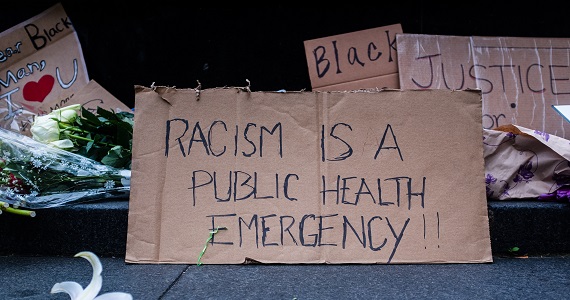 Cardboard sign with the phrase "Racism is a public health emergency"
